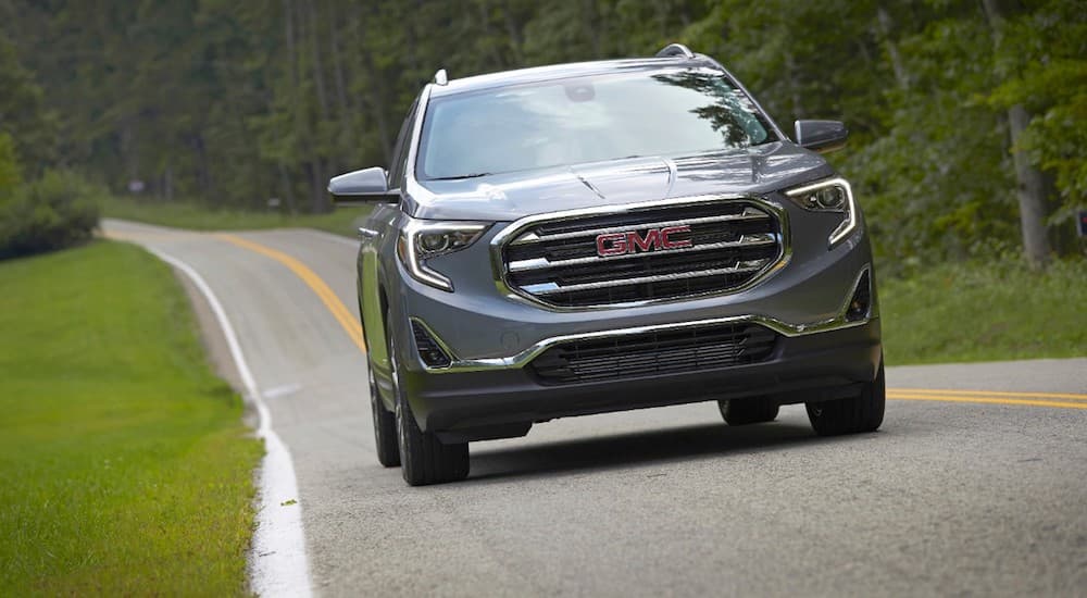 A blue GMC Terrain, which wins when comparing the 2019 GMC Terrain vs 2019 Ford Escape, is on a treelined road.