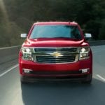 The front end of a 2020 Chevy Tahoe is driving on a treelined highway.