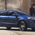 A blue 2020 Ford Edge, similar to ones that you'll find at your local car dealers, is driving on a city street.