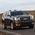 A black 2017 GMC Yukon, which is one of the best used SUVs for sale, is driving on a grass lined road.