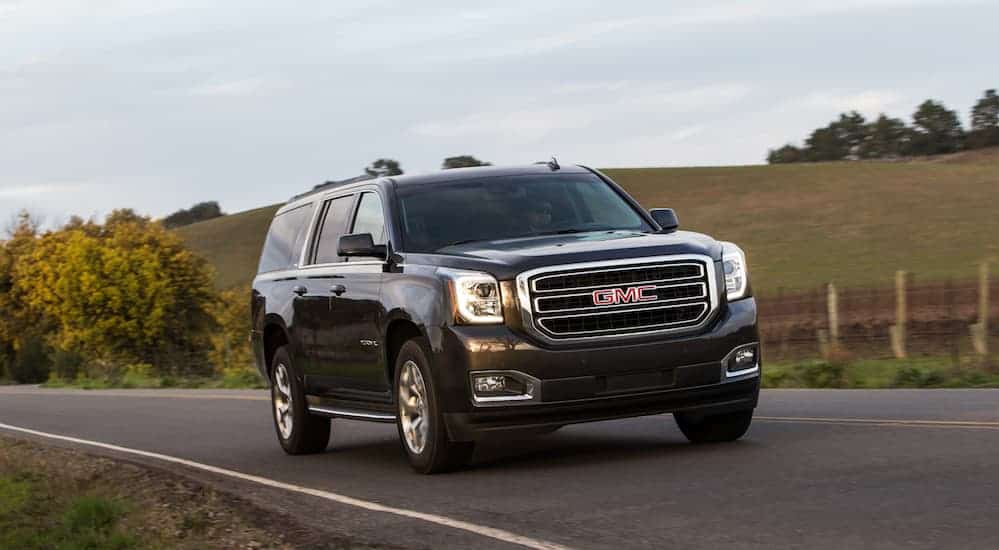 A black 2017 GMC Yukon, which is one of the best used SUVs for sale, is driving on a grass lined road.
