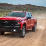 A red 2019 Chevy Silverado Trail Boss is driving on a dirt road while leaving a dirt cloud behind it.