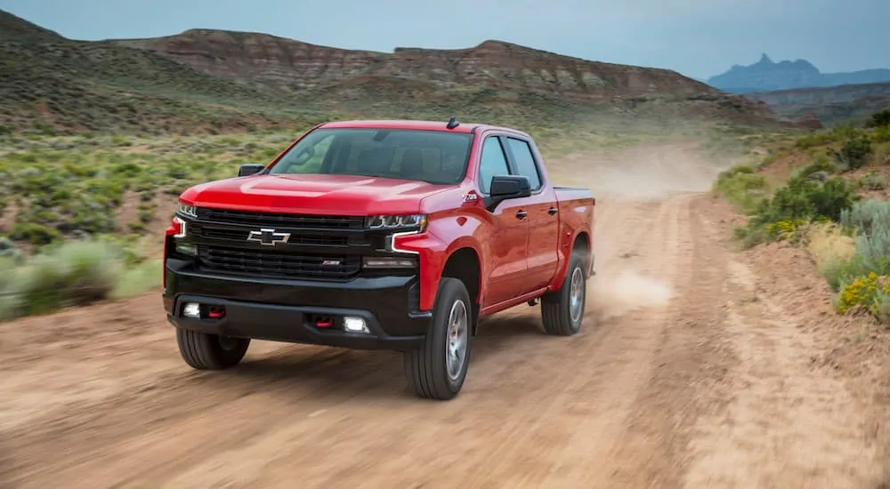 A red 2019 Chevy Silverado Trail Boss is driving on a dirt road while leaving a dirt cloud behind it.