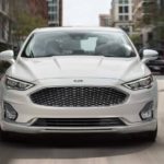 A white 2019 Ford Fusion is driving on a city street.