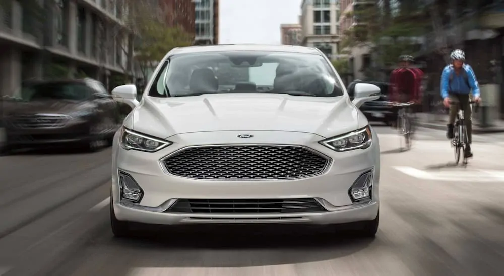 A white 2019 Ford Fusion is driving on a city street.