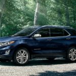 A blue 2020 Chevy Equinox is parked in a driveway with trees behind it.