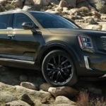 A forest green 2020 Telluride, which wins when comparing the 2020 Kia Telluride vs 2020 Subaru Ascent, is driving over rocks on a dirt trail.