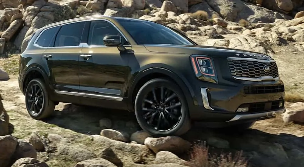 A forest green 2020 Telluride, which wins when comparing the 2020 Kia Telluride vs 2020 Subaru Ascent, is driving over rocks on a dirt trail.