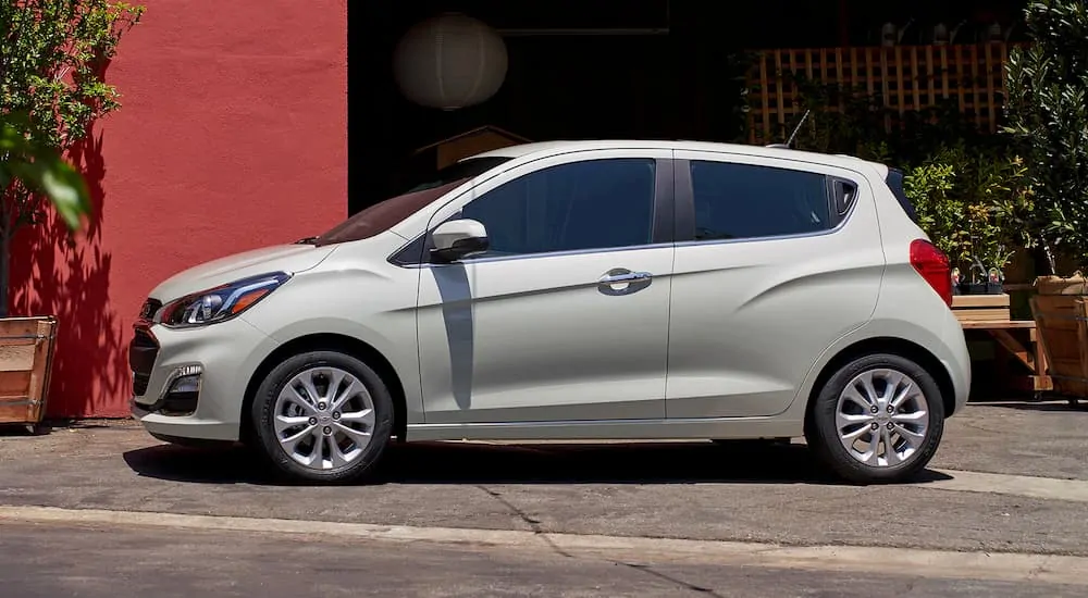 A white 2019 Chevy Spark, popular among used cars, is parked in front of a red building.
