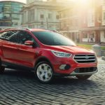 A red 2019 Ford Escape is driving through a town with cobble streets.