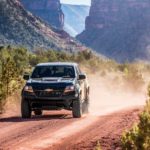 A black 2020 Chevy Colorado ZR2 is driving on a dirt road with a dirt cloud behind it.