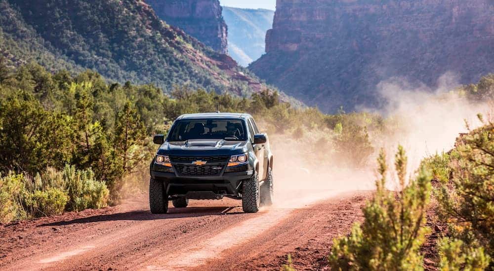 A black 2020 Chevy Colorado ZR2 is driving on a dirt road with a dirt cloud behind it.