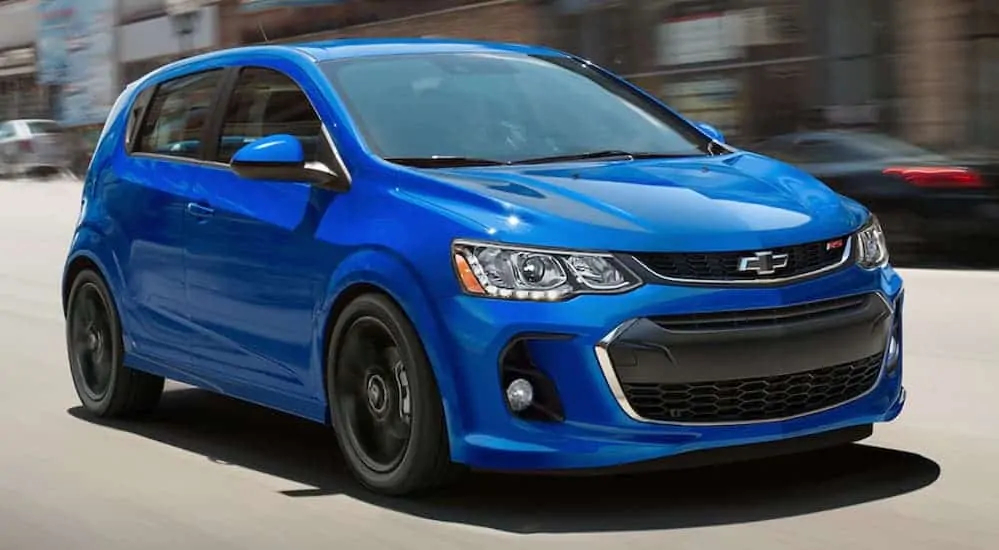 A blue 2020 Chevy Sonic is driving on a city street past blurred buildings.