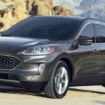 A grey 2020 Ford Escape is driving on a dirt road with mountains in the background.