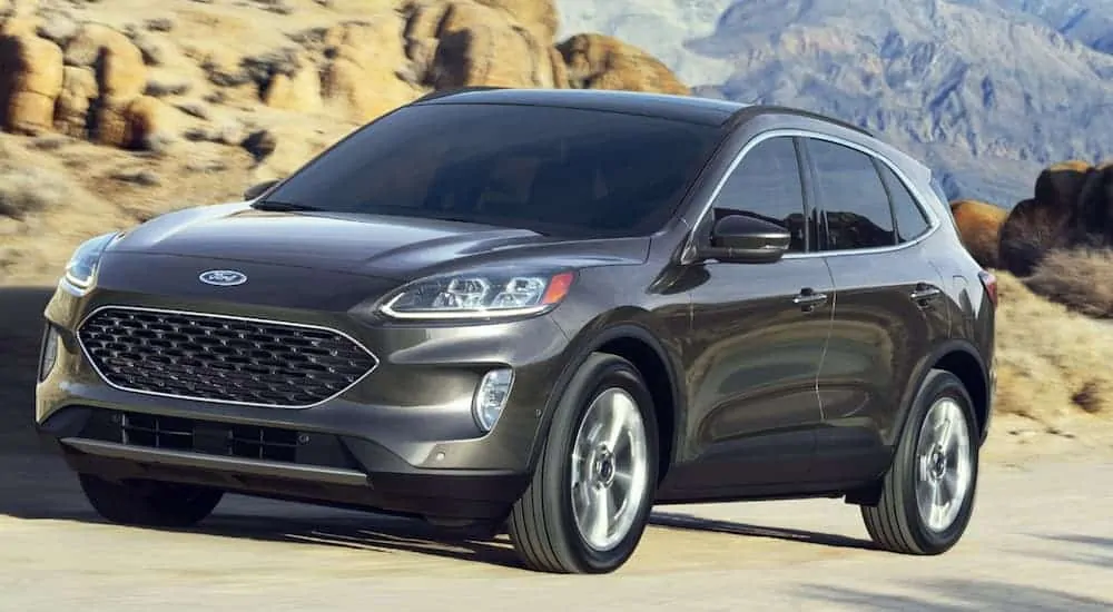 A grey 2020 Ford Escape is driving on a dirt road with mountains in the background.