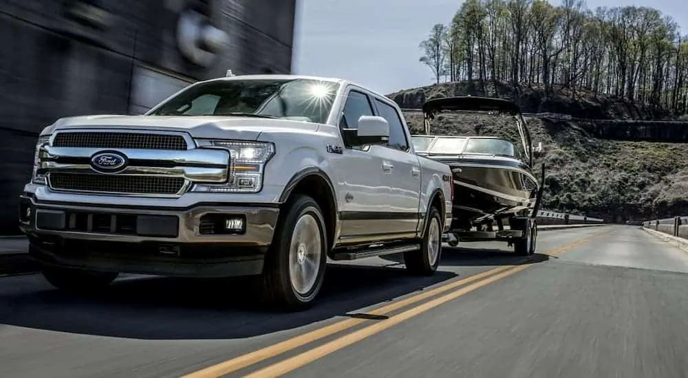 A white 2020 Ford F-150, which wins when comparing the 2020 Ford F-150 vs 2020 Ram 1500 is towing a boat.