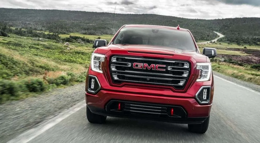 A red 2020 GMC Sierra 1500, which wins when comparing the 2020 GMC Sierra 1500 vs 2020 Nissan Titan, is driving with hills in the distance.