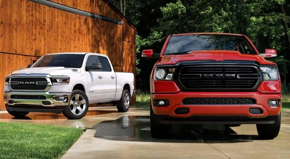 A white 2020 Ram 1500 is parked behind a red one on a driveway.