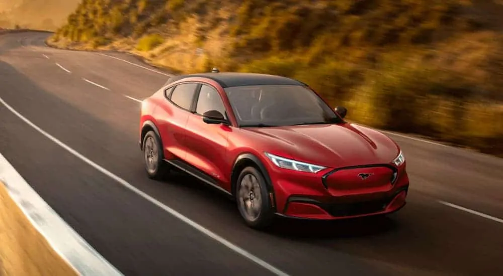 A red 2021 Ford Mustang Mach-E is driving on a grass lined road.