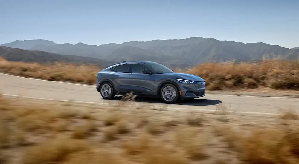 A grey 2021 Mustang Mach-E is driving with mountains in the distance.