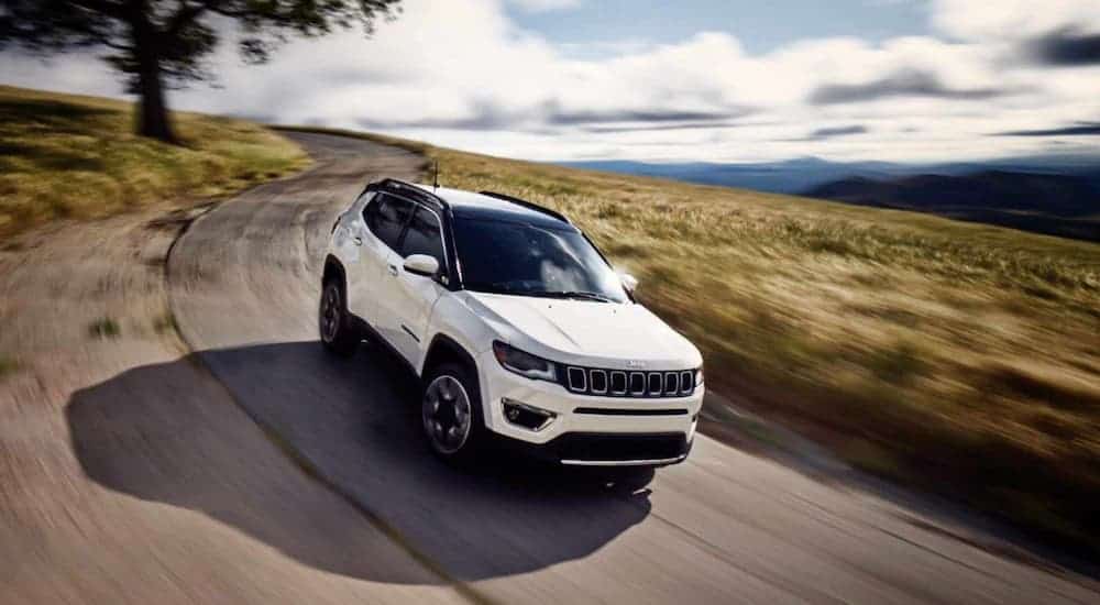 A white 2019 Jeep Compass is driving on a narrow, curvy road after leaving a Jeep dealership.