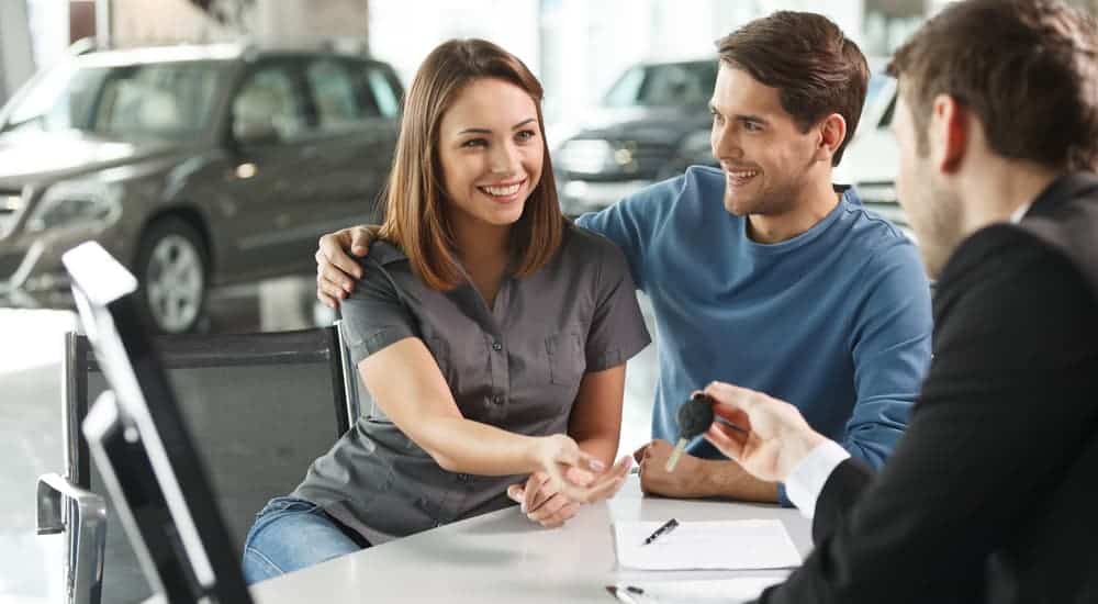 A car salesman is handing a couple the keys to the used car they purchased.