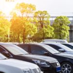 A row of used cars for sale are parked at a used car lot with a sun glare.