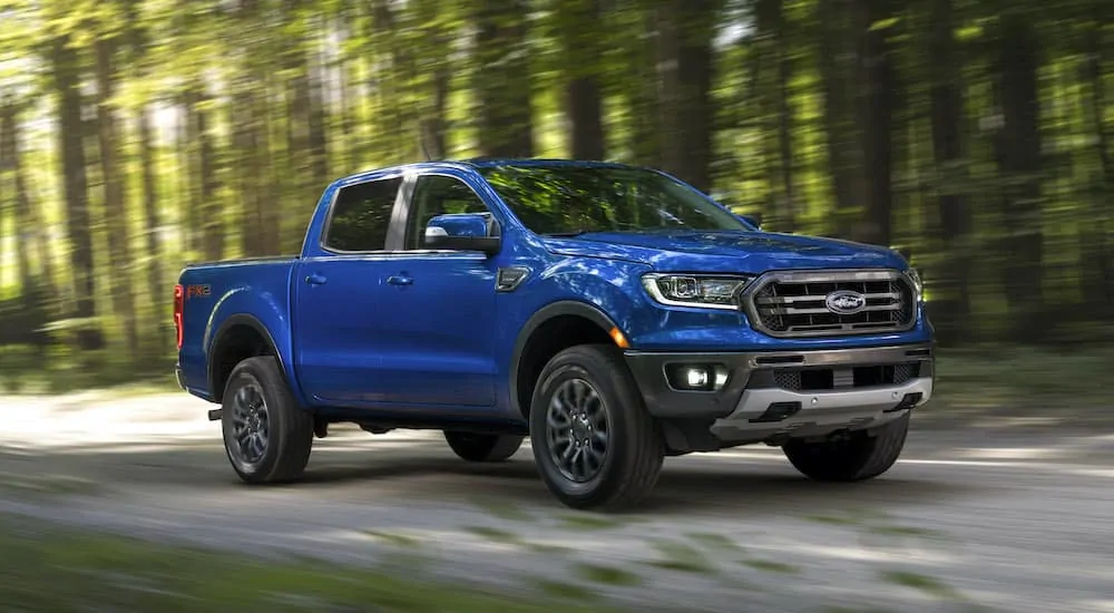 A blue Ford Ranger FX2 driving down a dirt road in a shadowy forest.