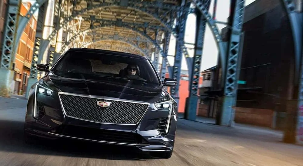 A black 2020 Cadillac CT6 is driving under a metal bridge while facing forward.