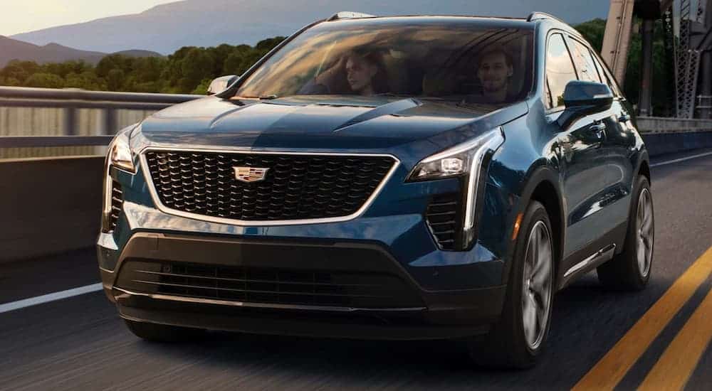 A blue 2020 Cadillac XT4, which wins when comparing the 2020 Cadillac XT4 vs 2020 BMW X1, is driving over water while on a bridge.