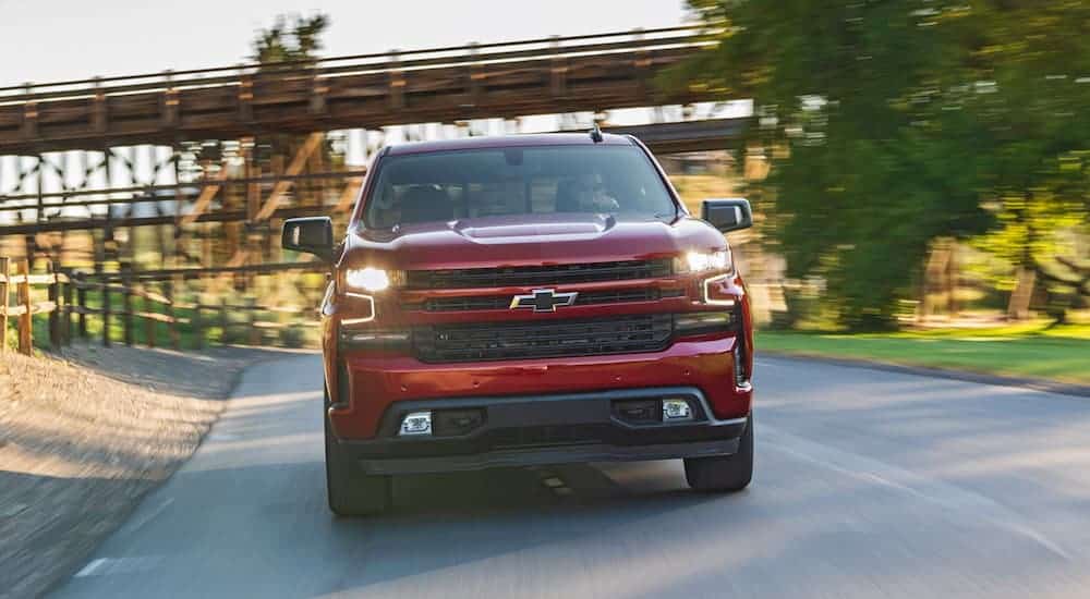 A red 2020 Chevy Silverado 1500 is driving on a tree lined road while facing forward.