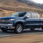 A blue 2020 Chevy Silverado, which wins when comparing the 2020 Chevy Silverado vs 2020 Ford F-150, is driving on a brown grass lined road.