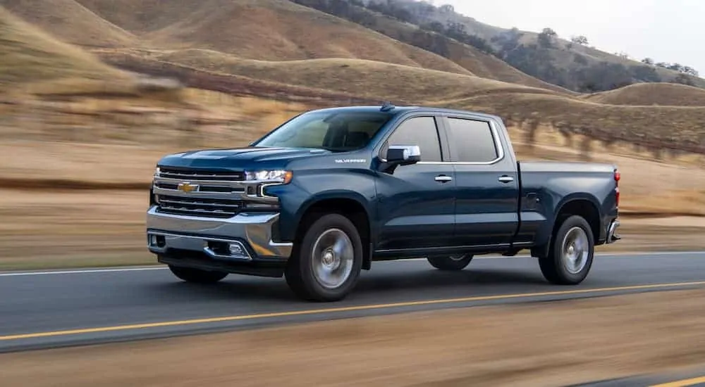 A blue 2020 Chevy Silverado, which wins when comparing the 2020 Chevy Silverado vs 2020 Ford F-150, is driving on a brown grass lined road.