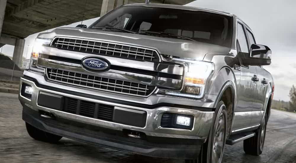 A silver 2020 Ford F-150 is driving under a bridge.