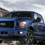 A blue 2020 Ford F-150 is parked on grass with a mountain in the distance.