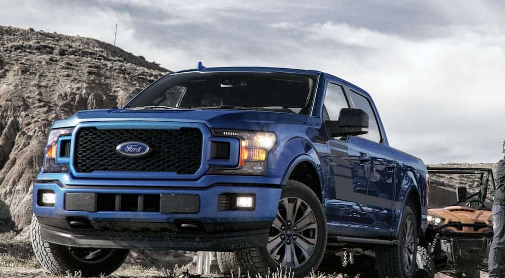 A blue 2020 Ford F-150 is parked on grass with a mountain in the distance.