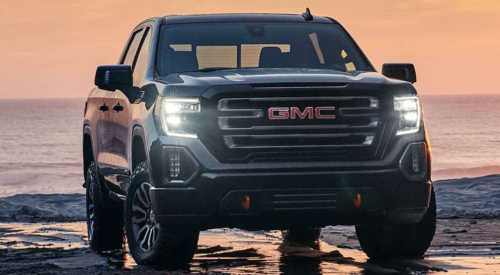 A black 2020 GMC Sierra is parked on a beach while the sunsets behind it.