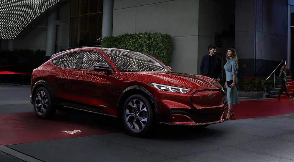 A red 2021 Ford Mustang Mach-E is parked on a red carpet while in front of a restaurant at night.