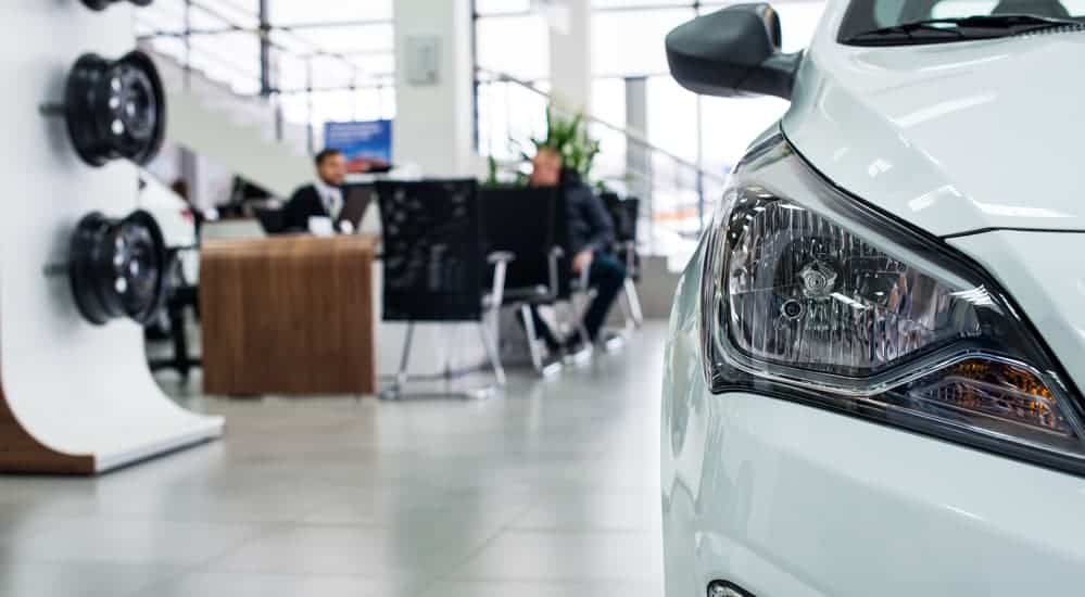 A close up of a white car is shown while parked in a car dealership's showroom.