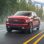 A popular Chevy diesel truck for sale near you, a red 2020 Chevy Silverado 1500 diesel, is driving on a misty forest highway.
