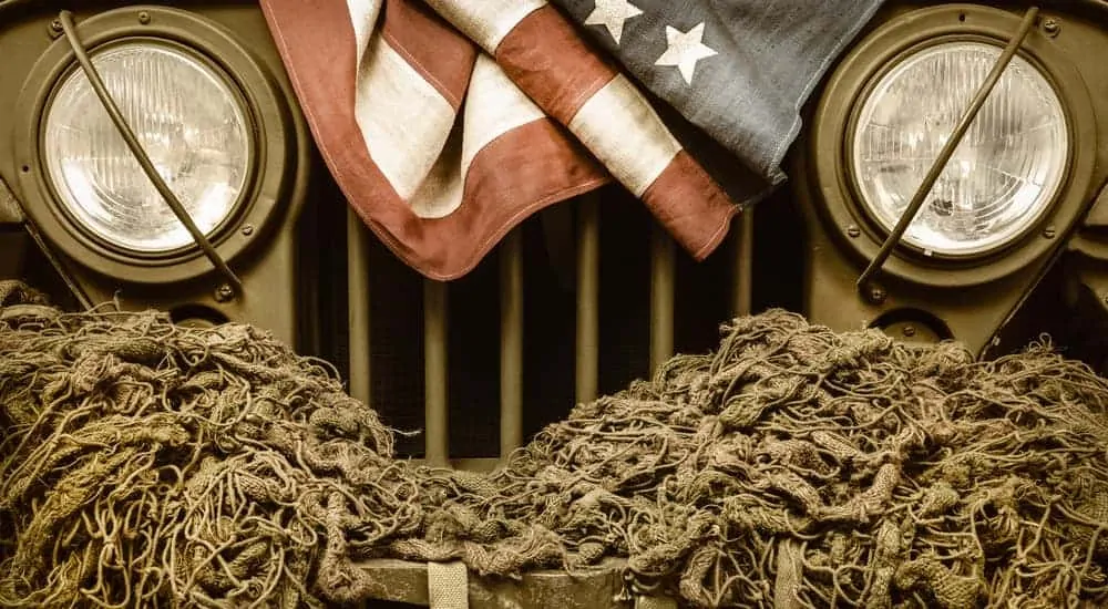 A close of a retro military Jeep grille is shown with a rope and an American flag on it.