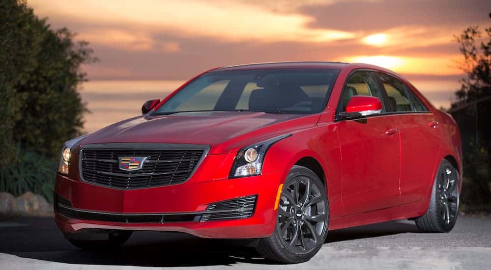 A red 2016 Cadillac ATS is parked in a road with a yellow sun set behind it.