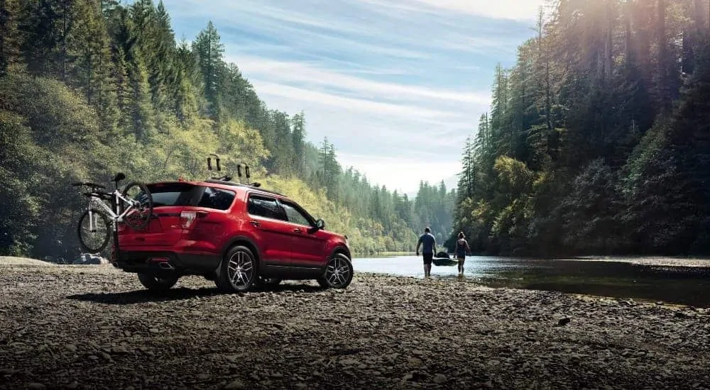 A red 2016 Ford Explorer is parked on a rocky shore while a couple brings a kayak to the water.