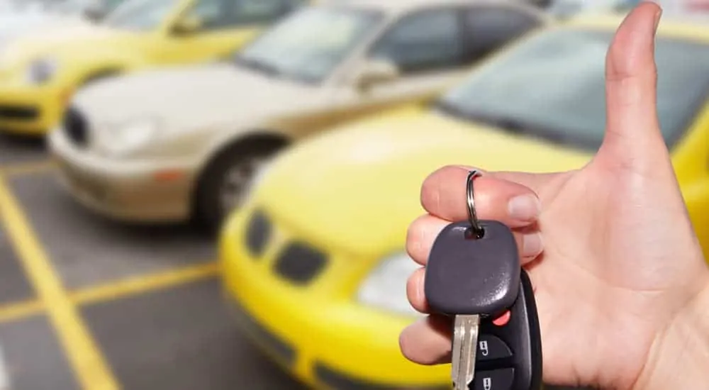 A hand is holding car keys to a used car while giving the thumbs up.