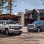 Two 2020 Chevy SUVs, a silver Suburban and grey Tahoe, are parked in front of a home.