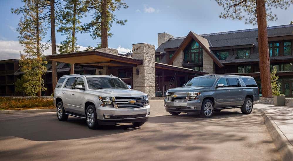 Two 2020 Chevy SUVs, a silver Suburban and grey Tahoe, are parked in front of a home.