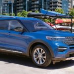 A blue 2020 Ford Explorer, which wins when comparing the 2020 Ford Explorer vs 2020 Honda Pilot, is parked next to a boat dock with kayaks behind it.