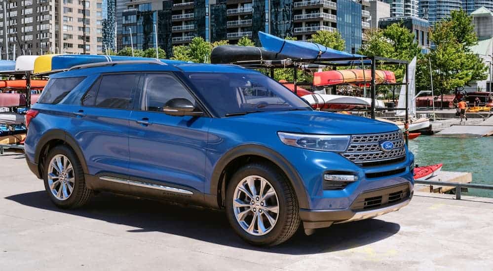 A blue 2020 Ford Explorer, which wins when comparing the 2020 Ford Explorer vs 2020 Honda Pilot, is parked next to a boat dock with kayaks behind it.