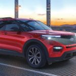 A red 2020 Ford Explorer, which wins when comparing the 2020 Ford Explorer vs 2020 Honda Pilot, is driving over a metal bridge at sunset.