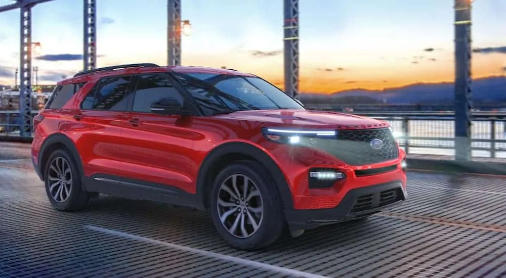 A red 2020 Ford Explorer, which wins when comparing the 2020 Ford Explorer vs 2020 Honda Pilot, is driving over a metal bridge at sunset.